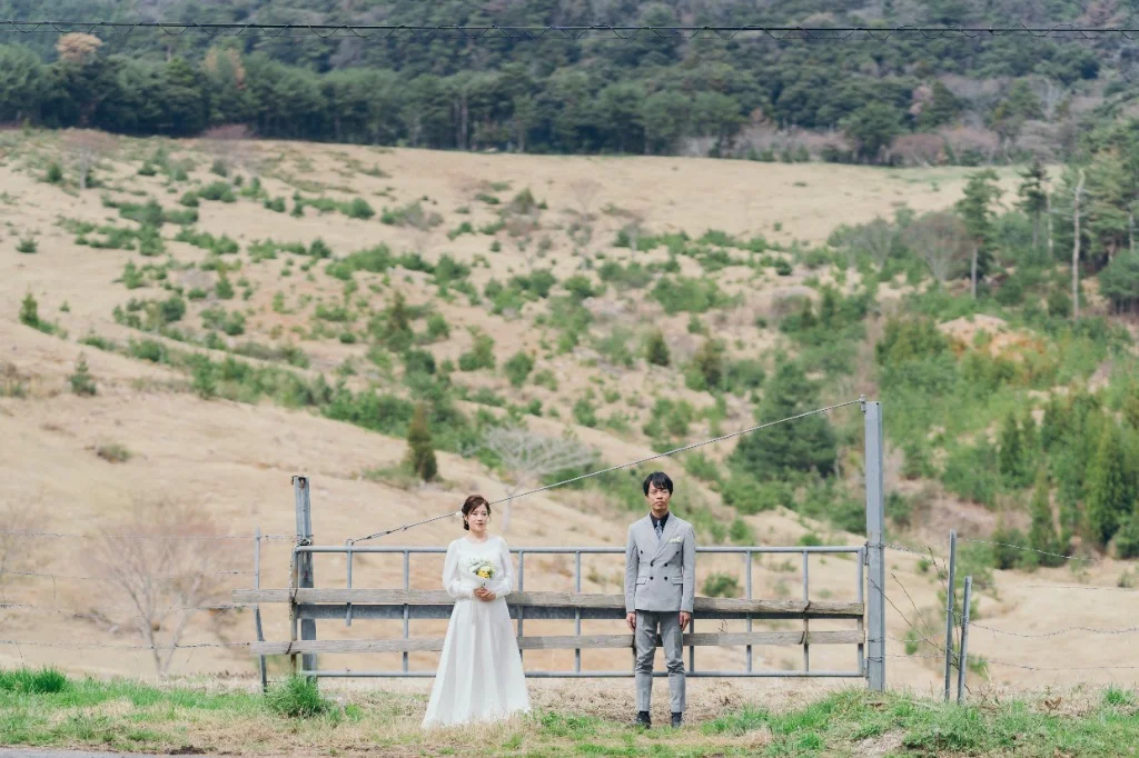 牧草地の丘のフェンス前に立つ新郎新婦
