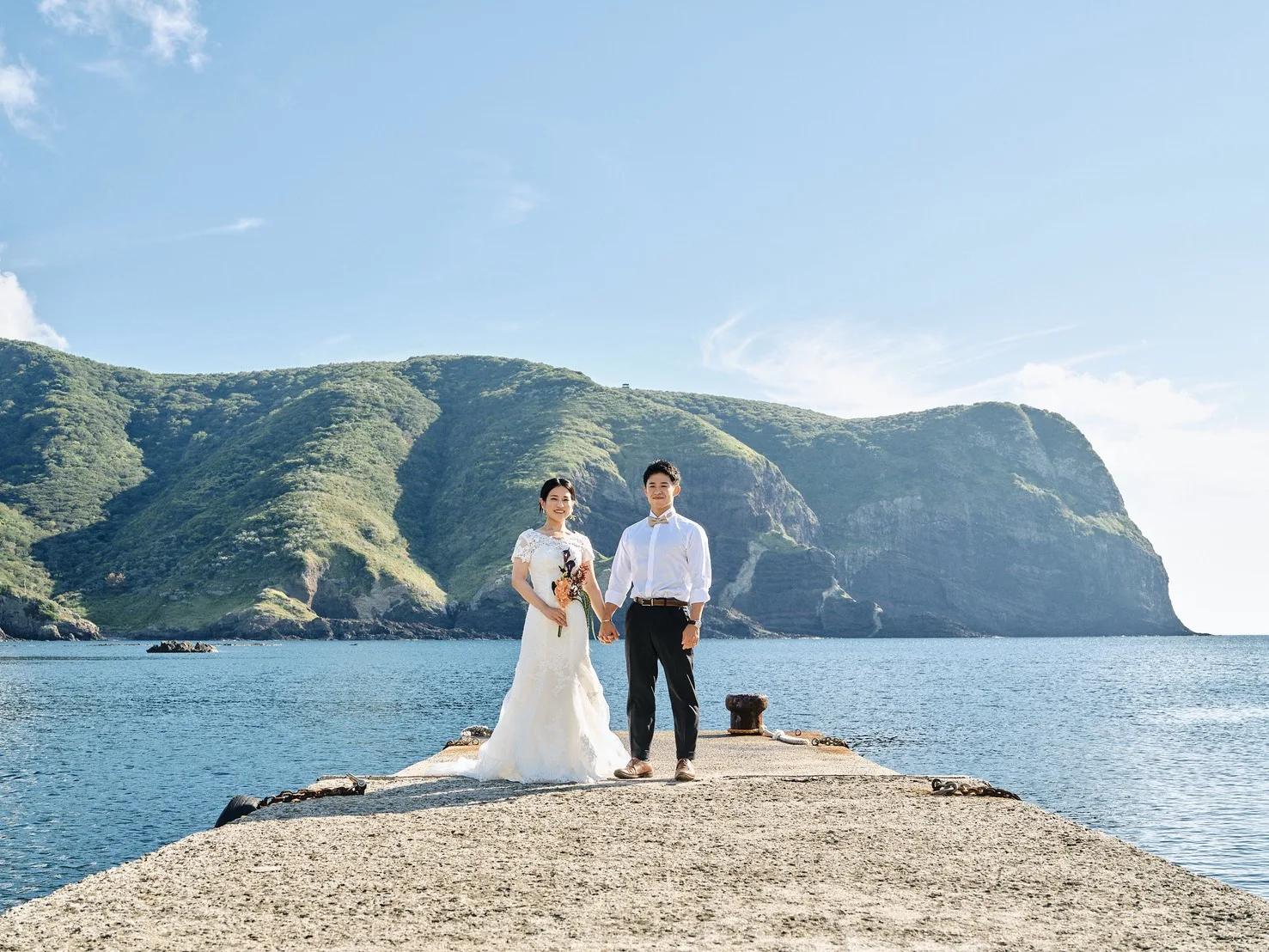 国賀海岸の突堤に立ち、崖を背景にする新郎新婦