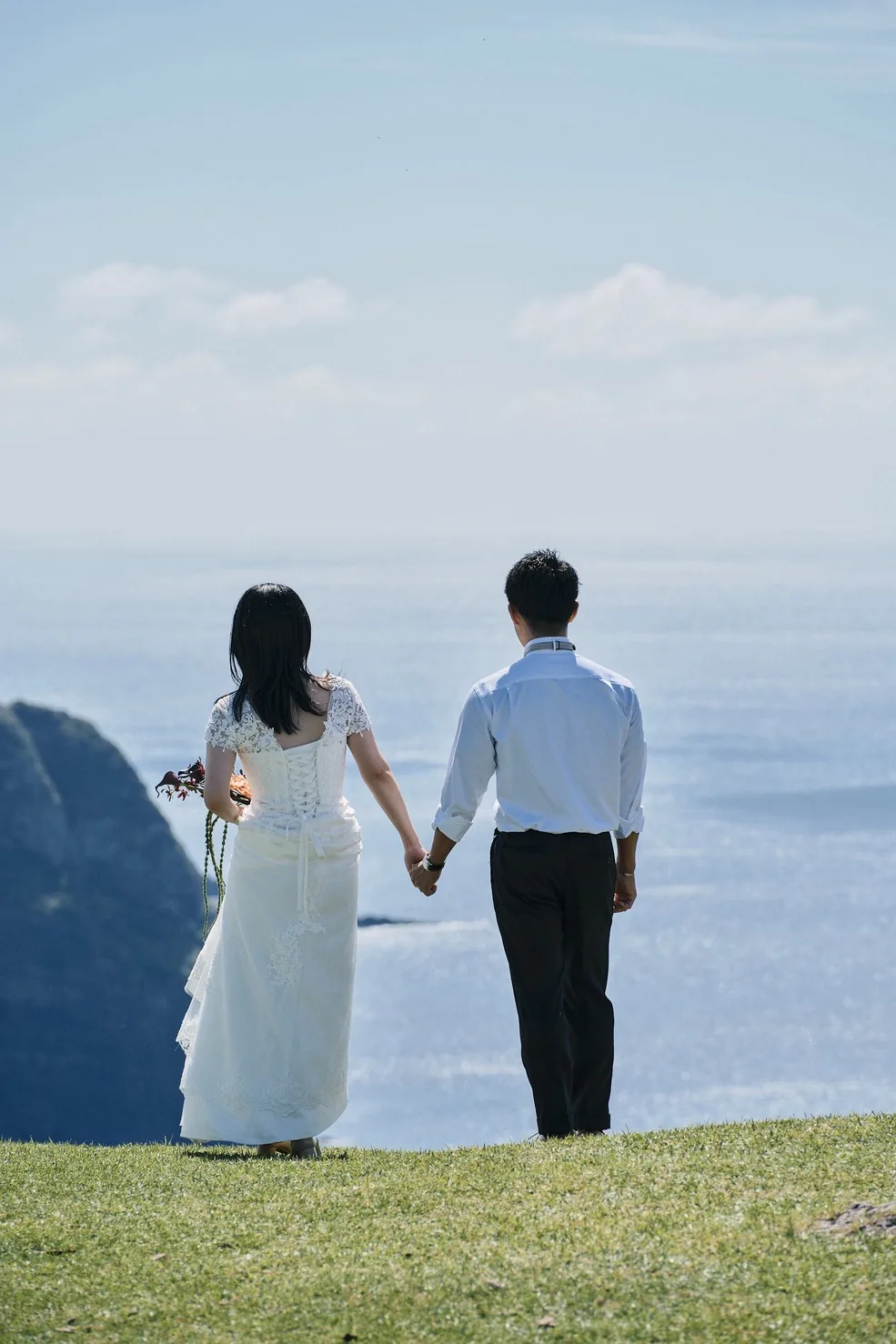 摩天崖の草原から海へ向かって歩く新郎新婦