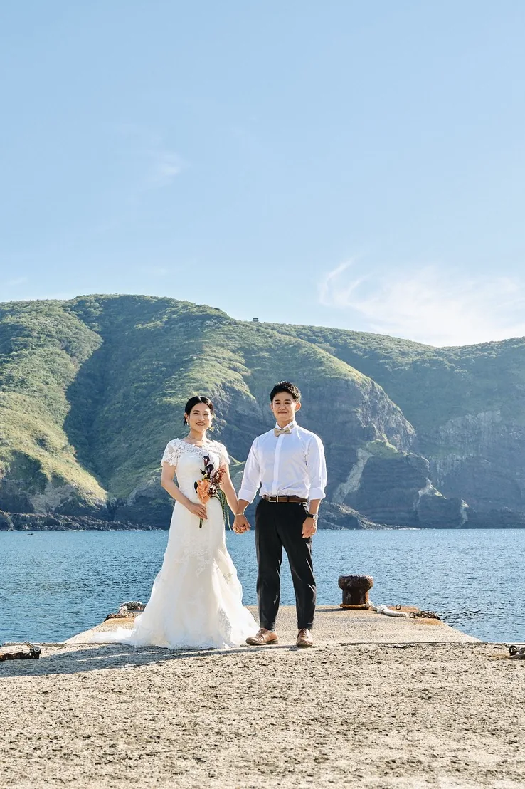 国賀海岸の突堤に立ち、崖を背景にする新郎新婦