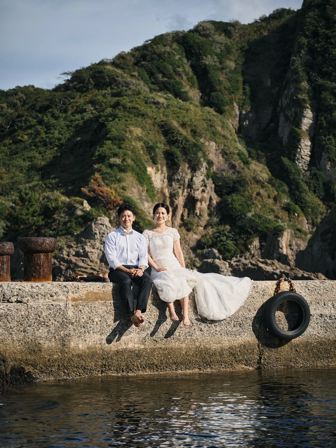 国賀海岸の突堤に腰かけ、裸足で座る新郎新婦
