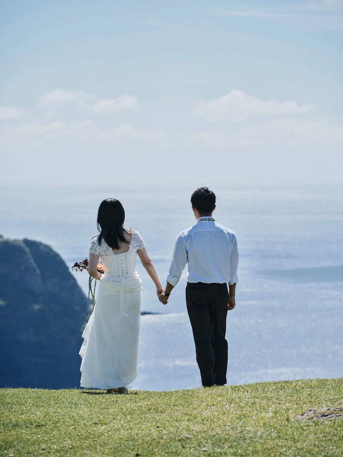 摩天崖から海を見下ろしながら歩く新郎新婦