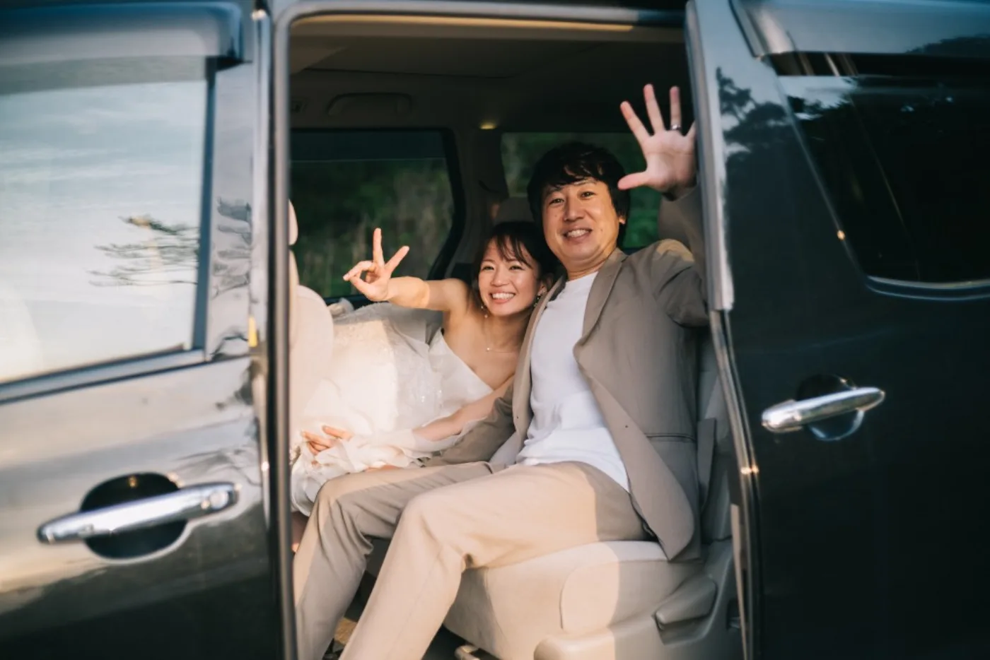移動中の車内で笑顔で手を振る新郎新婦