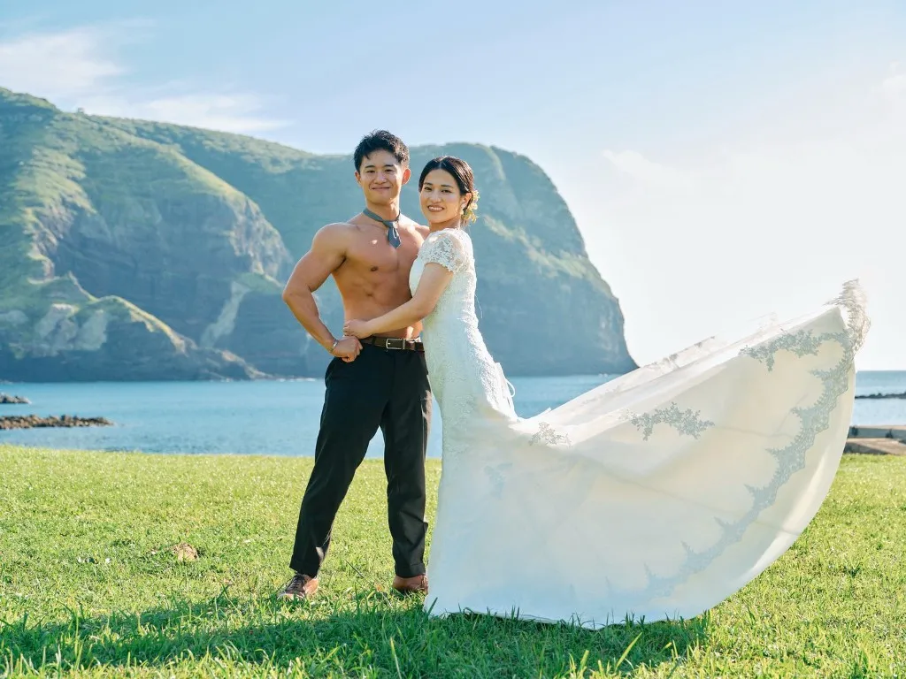 摩天崖の草原で、ドレスの裾が風に流れる新郎新婦